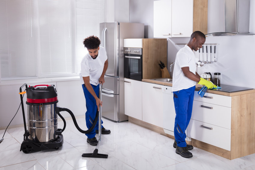 Two Young Male Janitor In Uniform Cleaning The Induction Stove And Floor In The Kitchen