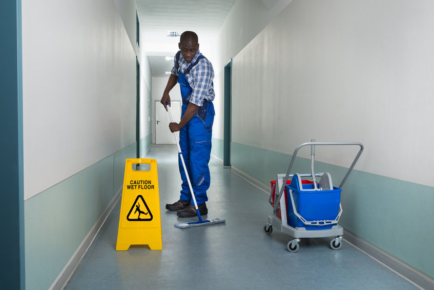 Young African Male Janitor Cleaning Floor In Corridor